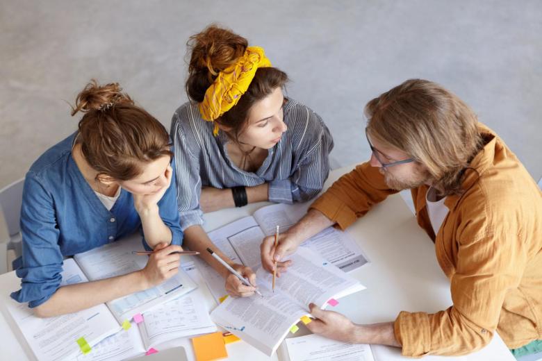 Photo de trois personnes assis à une table entrain de travailler sur un projet.